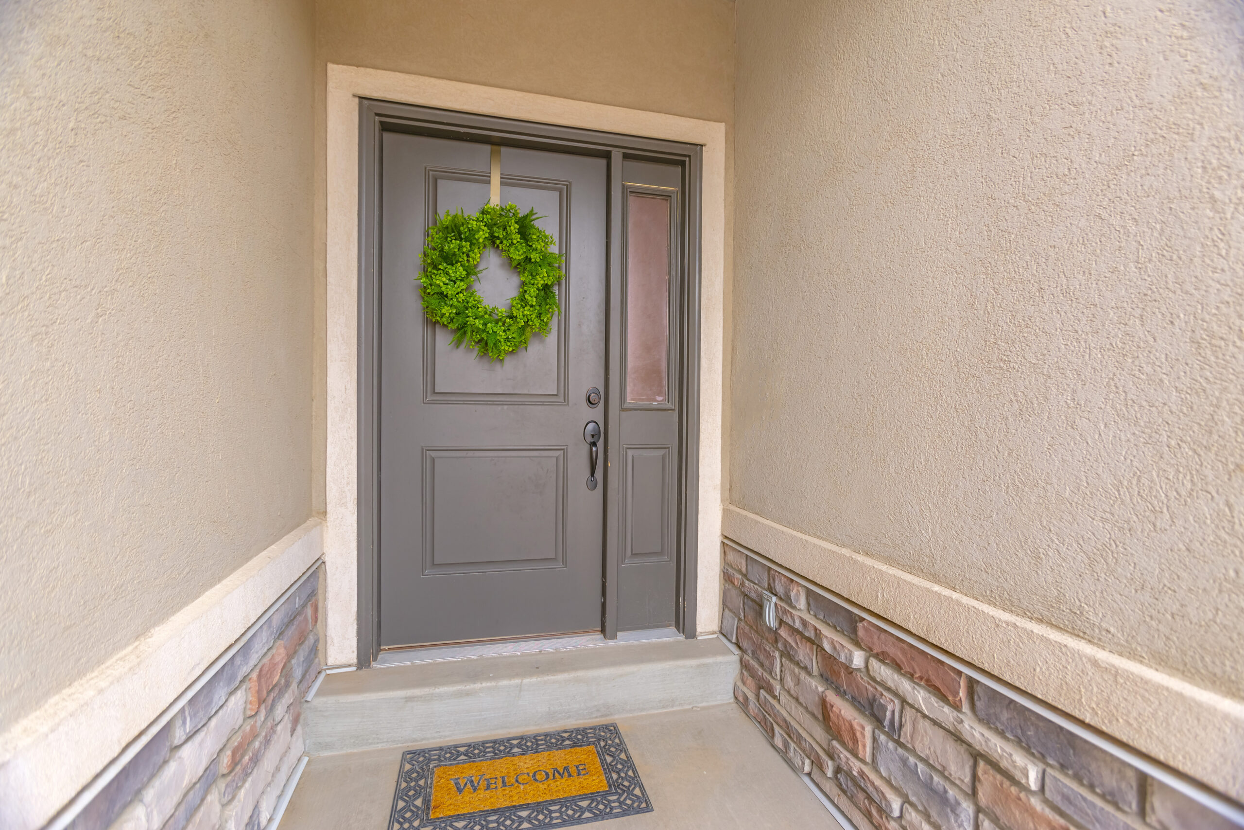 gray front door of a home with a simple green wreath and sidelight